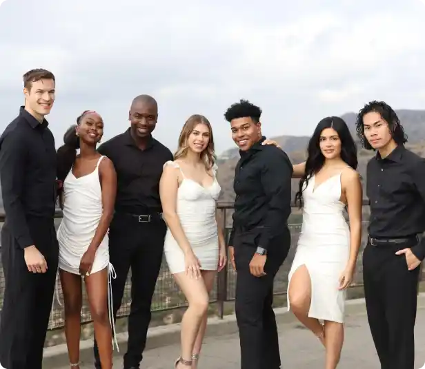 Seven Premier Staff members in formal attire, standing outdoors against a scenic backdrop of hills and clouds.