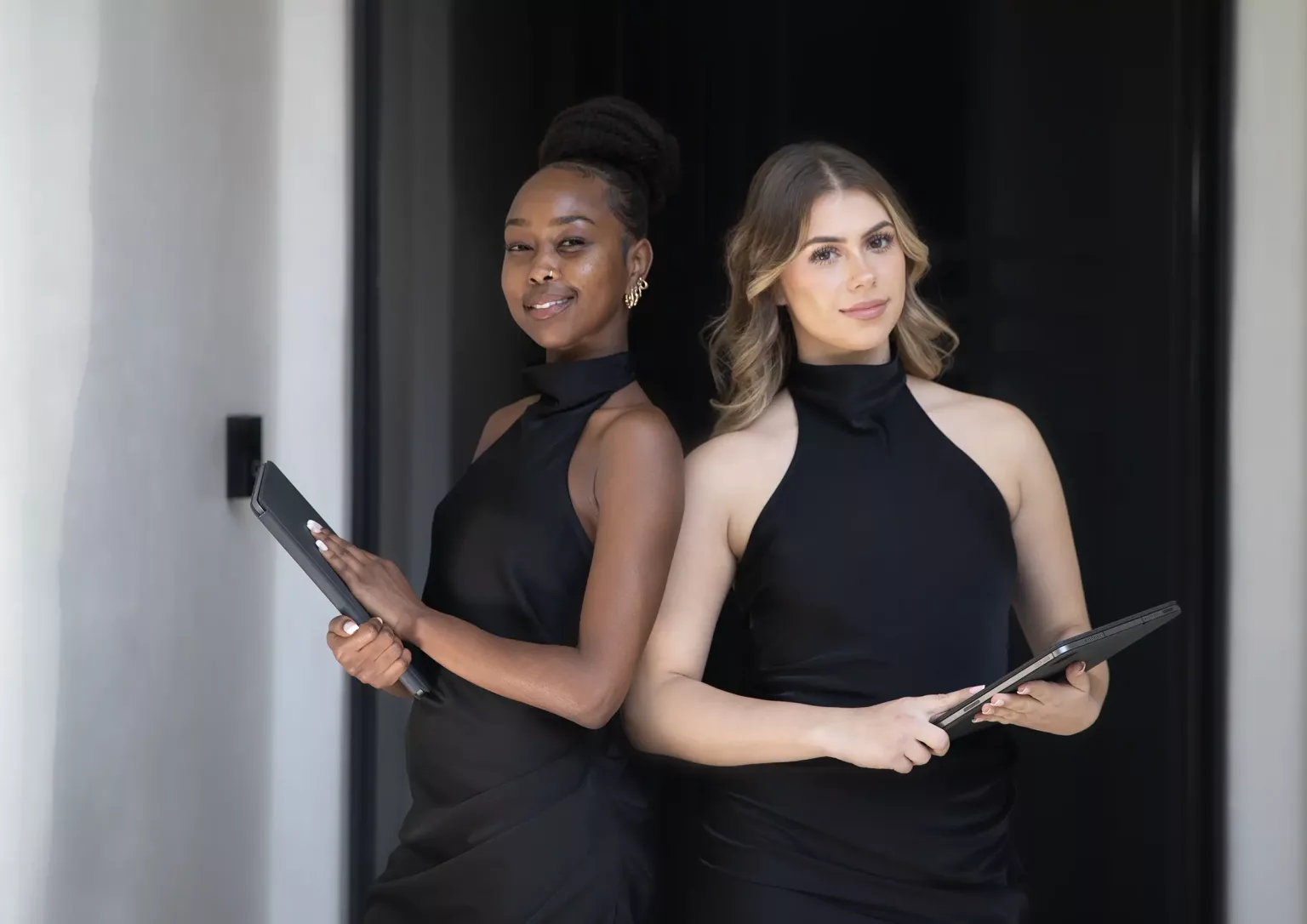 Two professional event staff in elegant black attire holding tablets, ready to assist at an event.