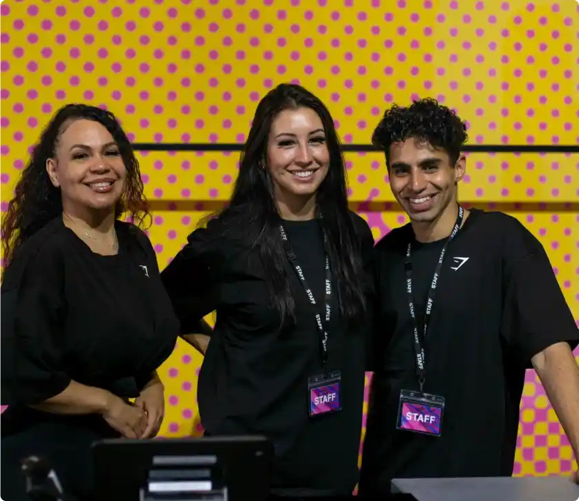 Premier Staff members standing in front of a vibrant yellow background with pink polka dots, wearing black shirts and staff badges, ready to assist at an event.